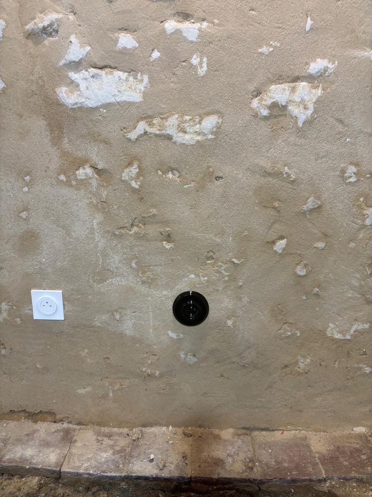 Prise ronde noire posée sur un mur en pierre et enduit à la chaux