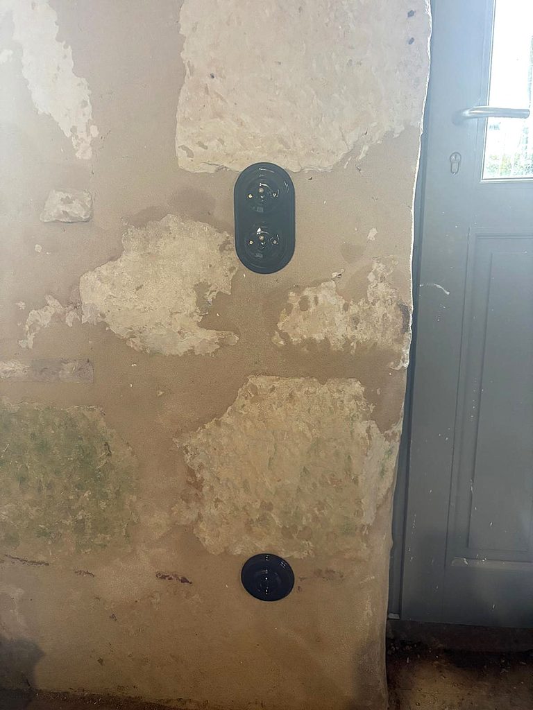 Prise ronde noire posée sur un mur en pierre et enduit à la chaux
